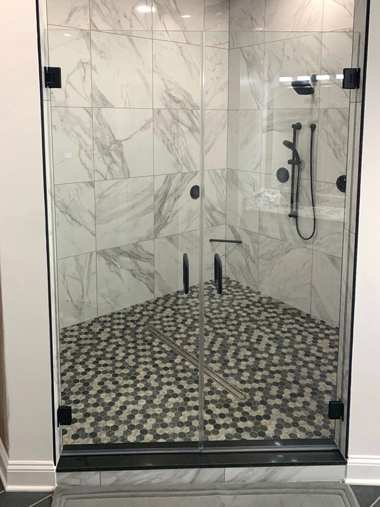 Frameless shower door with matte black hinges and a pebble tile floor